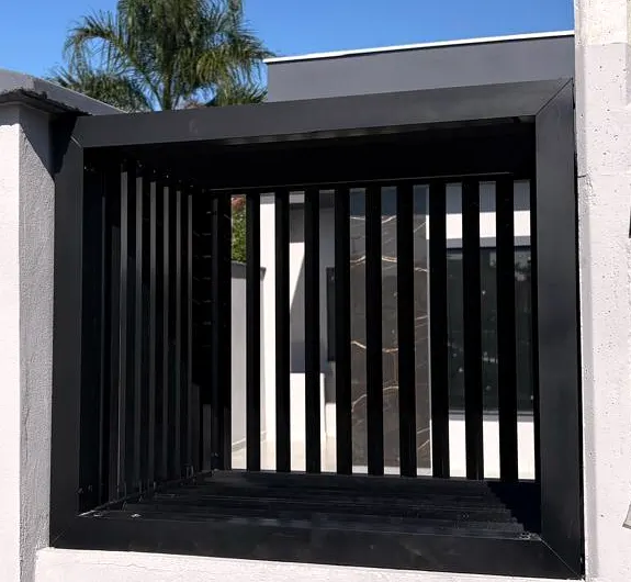 Abrigo de lixeira em ripado metálico preto embutido no muro branco de uma residência, ao lado do portão