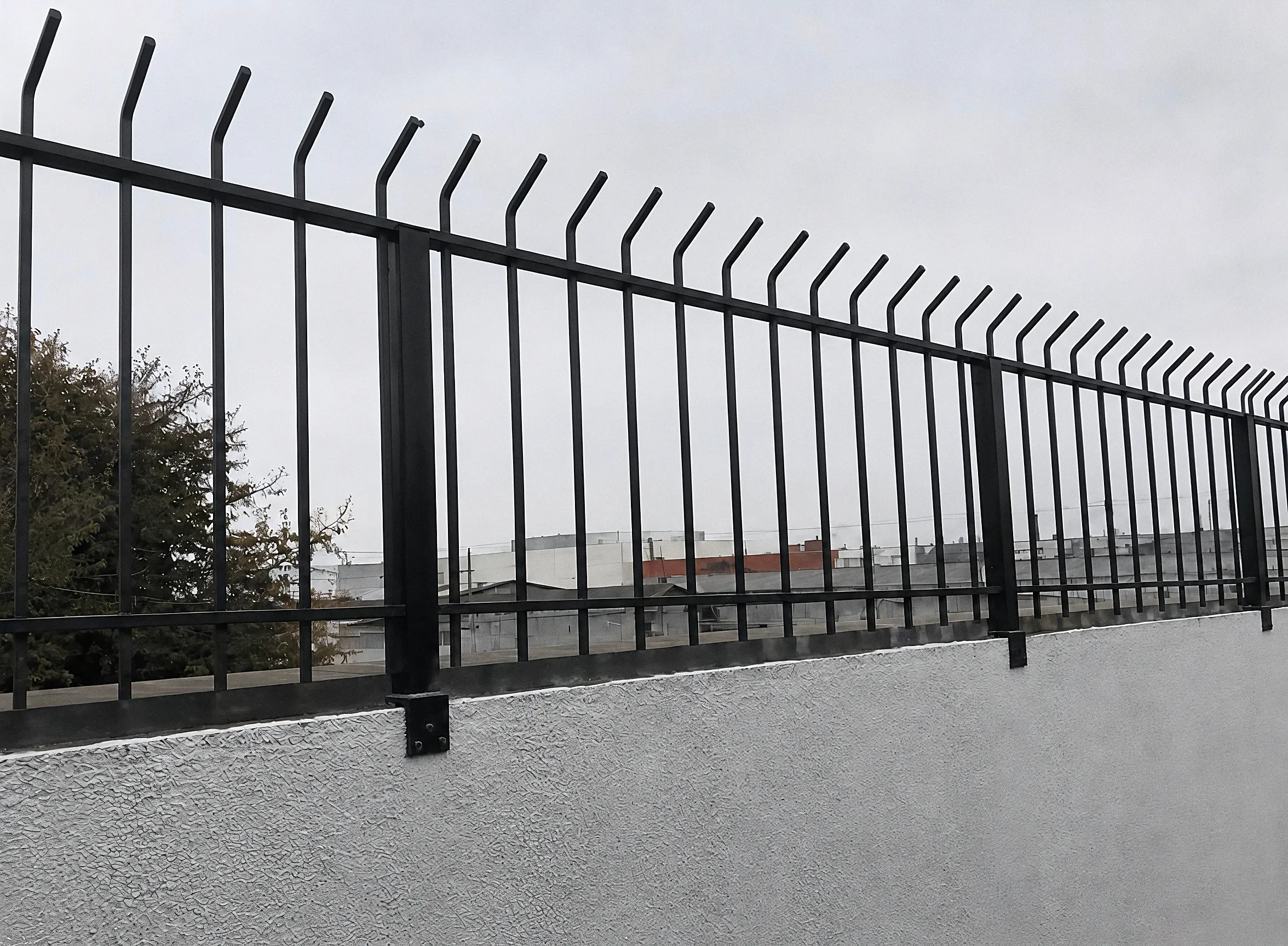 Gradil preto com pontas tipo lança sobre muro de concreto