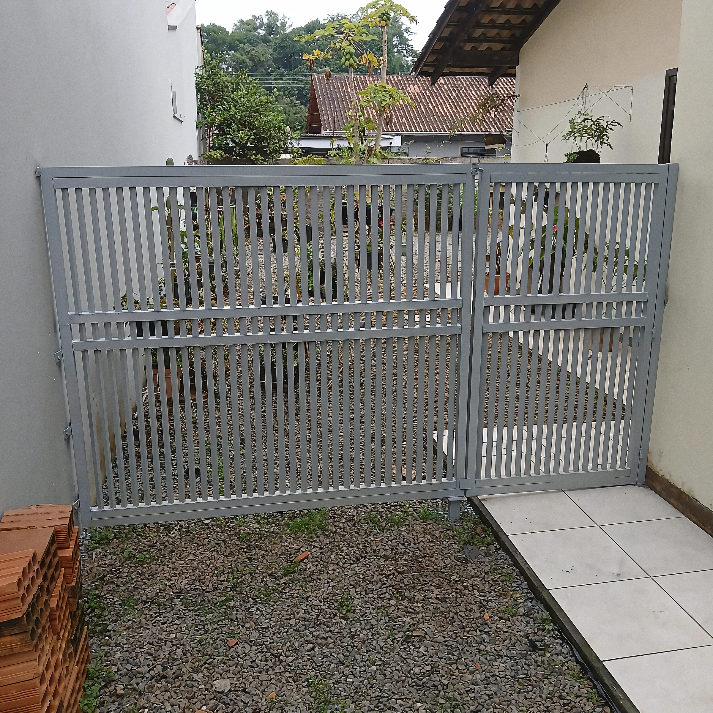 Portão duplo cinza com grade vertical e jardim ao fundo