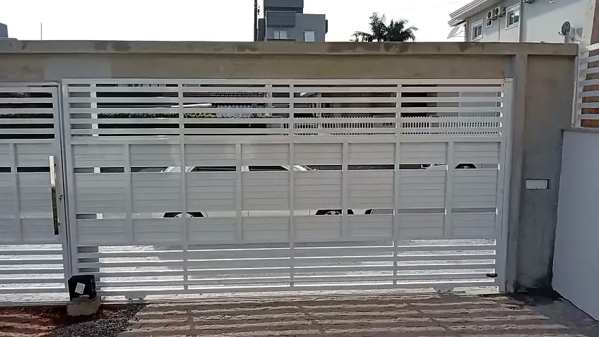 Portão de correr branco com ripas horizontais abrindo e fechando na garagem de uma residência