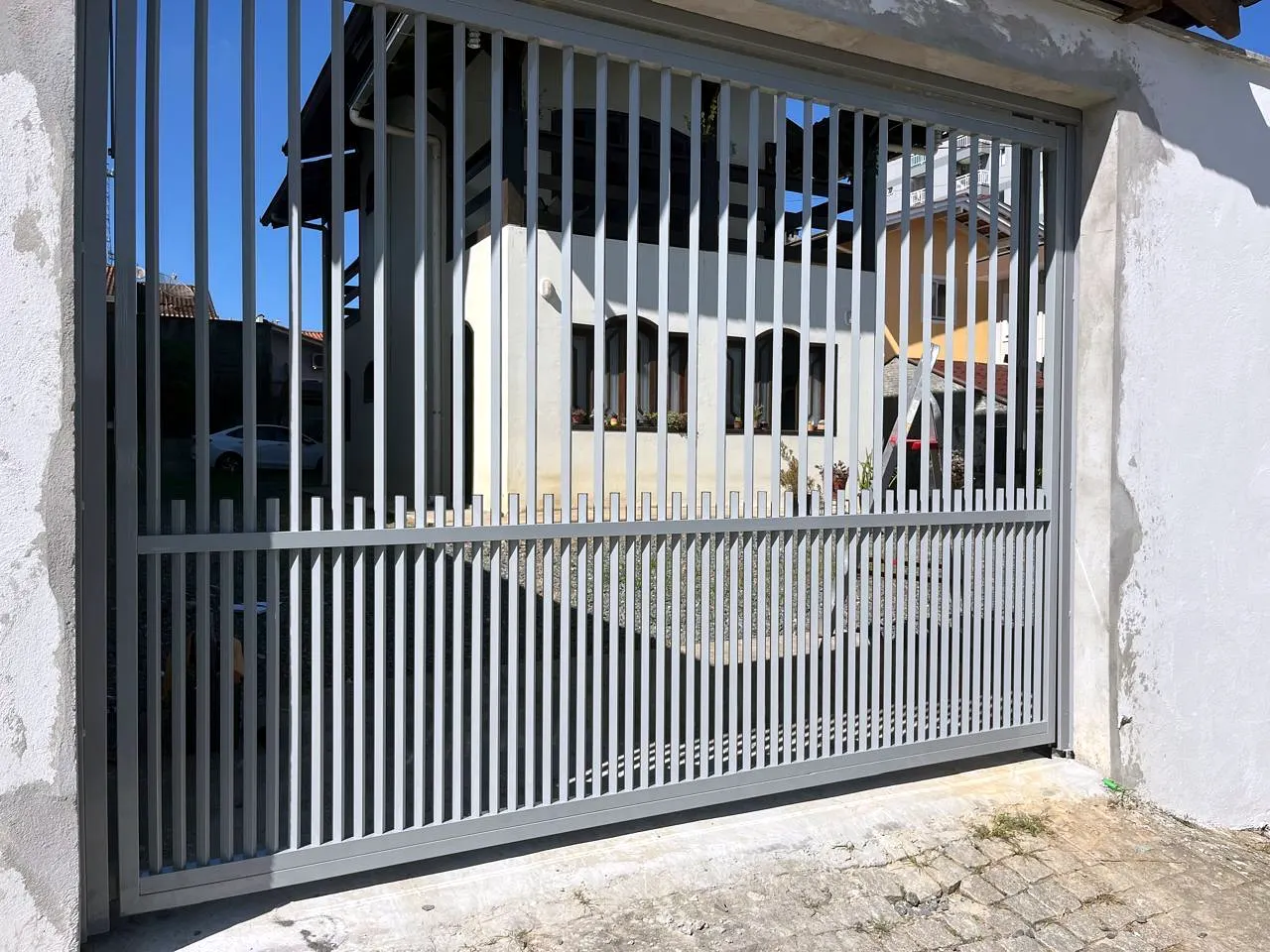 Portão de correr cinza com barras verticais e travessa no meio, instalado no vão de garagem de uma residência