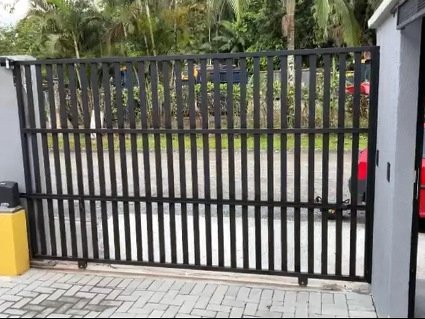 Portão de correr preto de barras verticais com automatizador montado em base amarela ao lado do trilho
