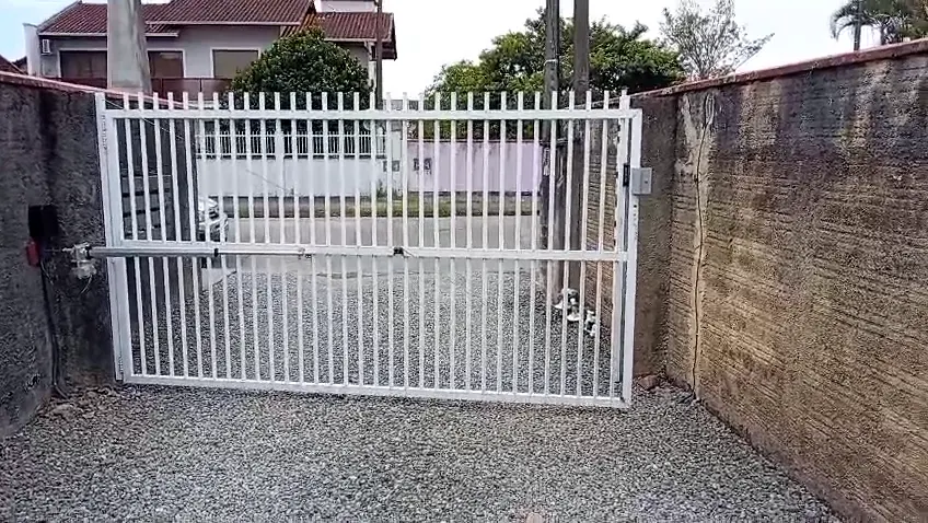 Portão pivotante branco de folha única, com motor e trava eletroímã, abrindo e fechando em residência no bairro Aventureiro, em Joinville
