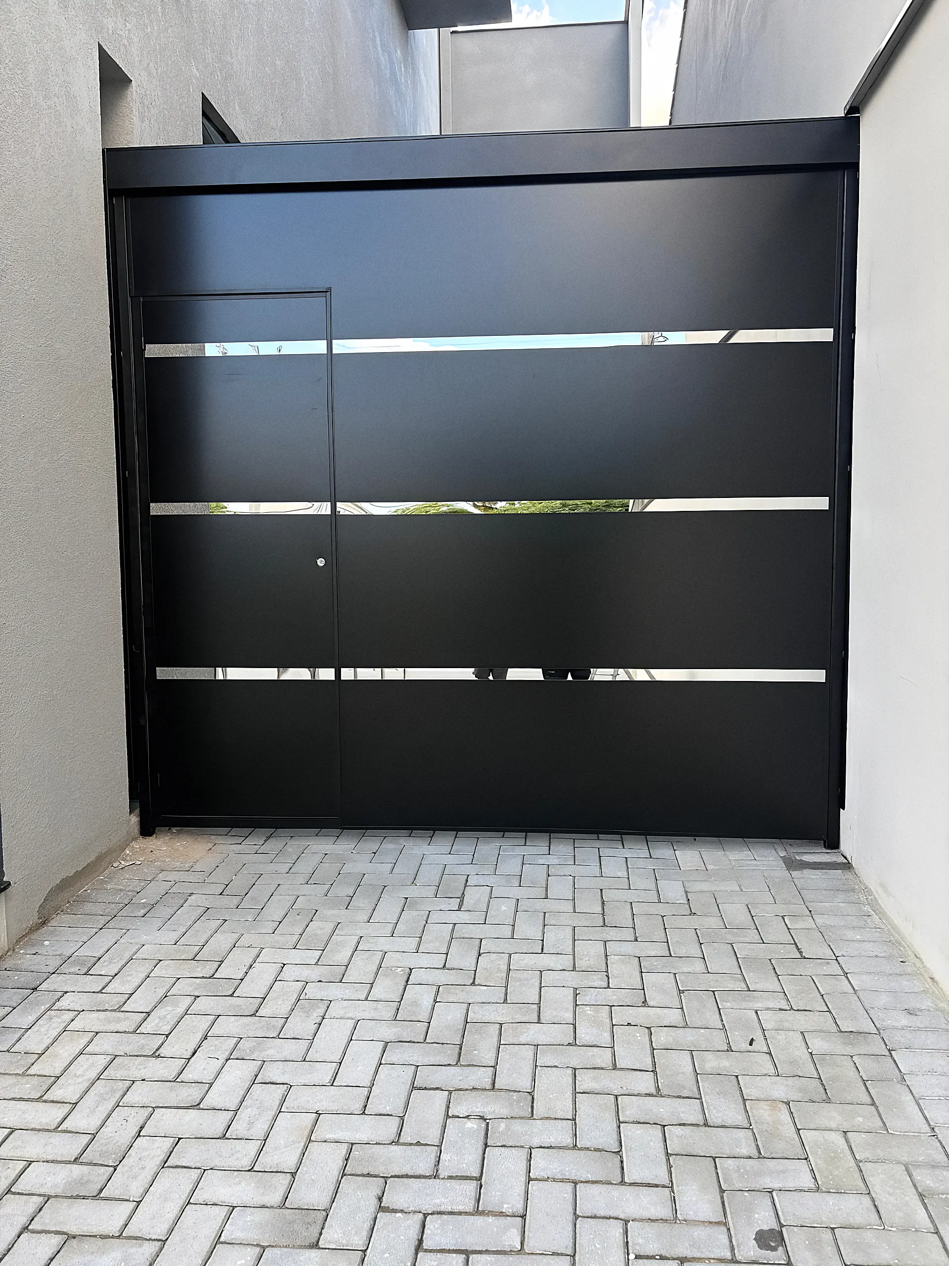 Portão de correr preto com três frisos horizontais sobre calçada de paver