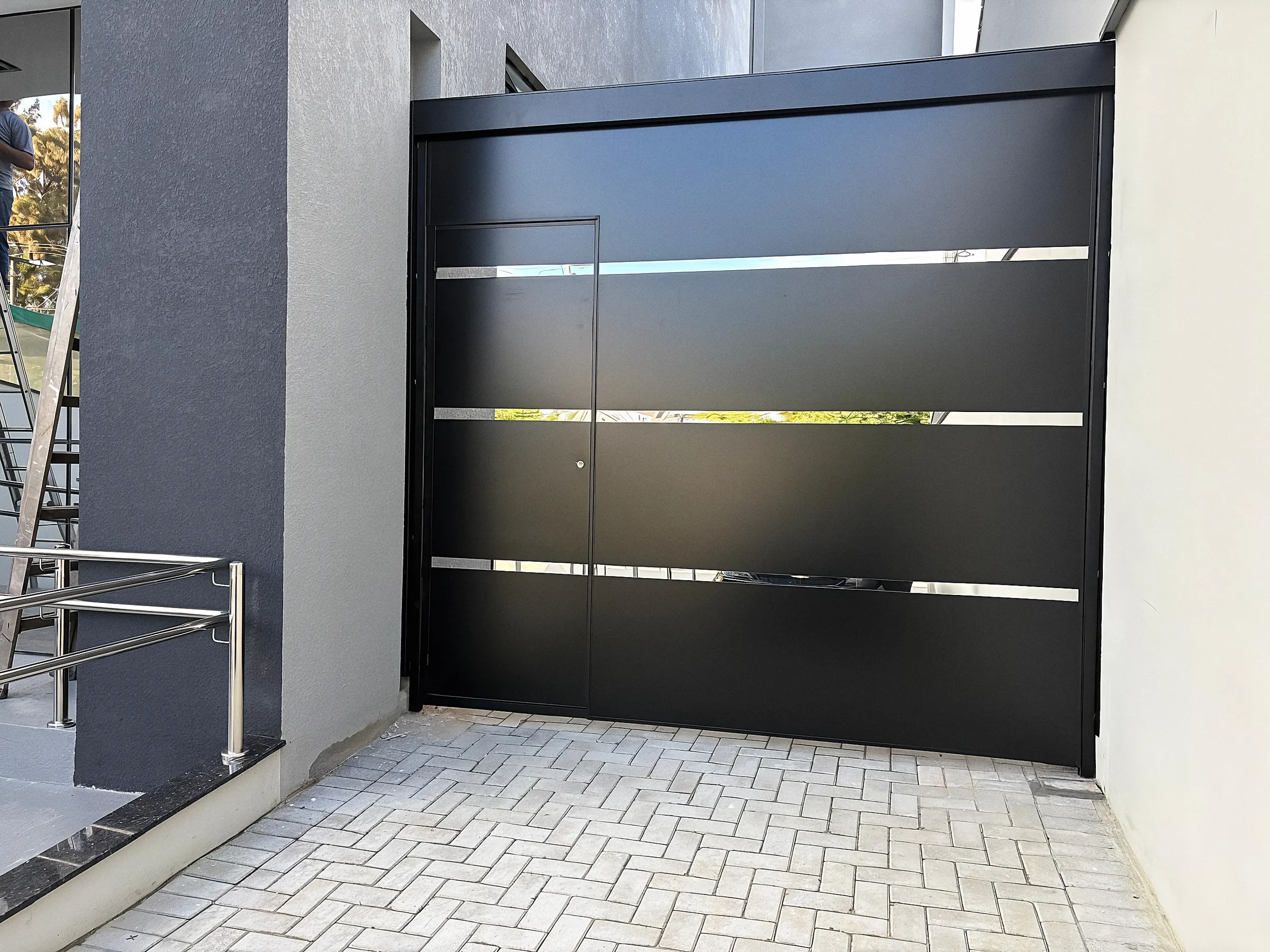 Portão de garagem preto com frisos horizontais vazados, instalado pela Elite Serviços