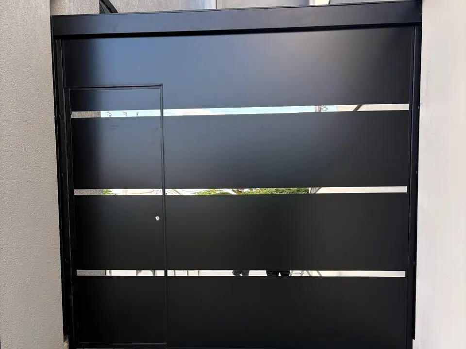 Portão de garagem em chapa preta com porta social embutida e três frisos horizontais vazados, feito pela Elite Serviços