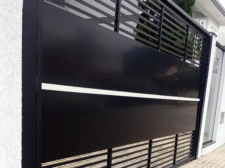 Portão ripado preto instalado em residência no Saguaçu, em Joinville/SC, com ripas horizontais vazadas em cima e embaixo, chapa lisa ao centro e friso claro atravessando o portão.